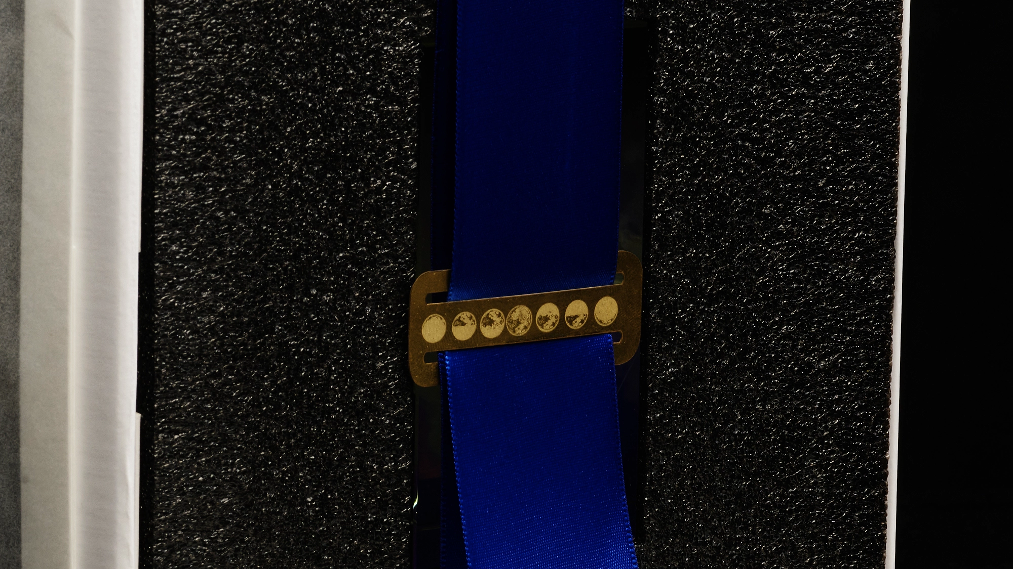 Moon-phase brass clasp holding the blue satin ribbon